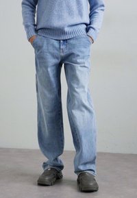 Light blue denim pants with a relaxed fit, featuring a straight leg design and side pockets, paired with dark shoes and a light blue sweater.