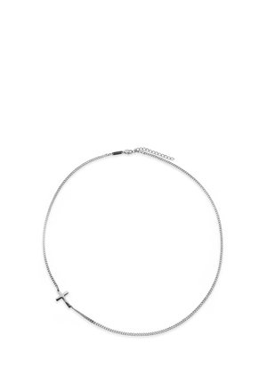 Sølvkjedet halskjede med et lite polert korsanheng plassert asymmetrisk på en hvit bakgrunn.