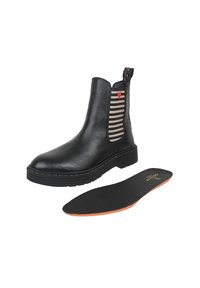 Czarne skórzane botki typu chelsea z paskiem elastycznym w paski po bokach oraz czerwonym detalem w kształcie serca; zawierają wyjmowaną czarną wkładkę. Gruba podeszwa i wyraziste szwy.