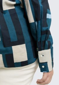 Langsleeve shirt in teal, marineblauw en crème met geometrische patronen. Knopf cuff en een relaxte pasvorm. Gemaakt van lichtgewicht stof.