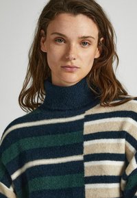 Maglione a collo alto a righe in navy, verde, crema e beige. Caratterizzato da ampie righe verticali di larghezze diverse con una consistenza morbida.
