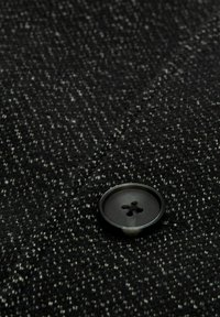 Zwart-witte houndstooth stof met een gestructureerd oppervlak, met een ronde zwarte knoop met vier gaten. Knoop is bevestigd aan de stof.