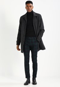 Grau Wolle Übermantel, schwarzer Rollkragenpullover, grüne karierte Hose und schwarze Stiefel. Schmal geschnittene, geknöpfte Jacke mit Seitentaschen und strukturiertem Stoff.