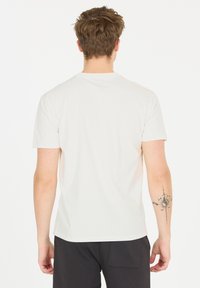 Vit bomull t-shirt med korta ärmar; har en rund halsringning och en slät yta. Svarta byxor med en bakficka. Synlig tatuering på armen.