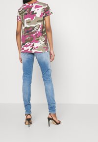 Kamouflage t-shirt i rosa, vitt och grönt, tillsammans med ljusblå skinny jeans och svarta högklackade sandaler. Korta ärmar och avslappnad passform.