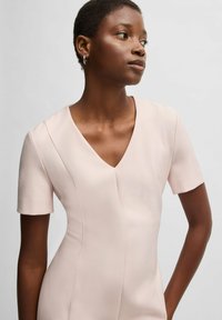 Abito aderente di colore rosa chiaro con maniche corte e scollo a V. Il tessuto ha una texture liscia e presenta dettagli delle cuciture eleganti.