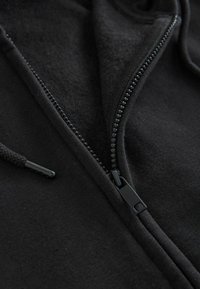 Sudadera con cremallera negra y un interior suave, con una cremallera lisa, cordones trenzados y un acabado de tejido texturizado.
