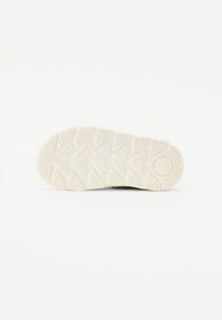Semelle de chaussure en caoutchouc blanc présentant un motif texturé avec des nervures en relief et un accent circulaire au niveau du talon.