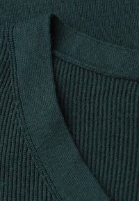 Tmavě zelená ribaná pletenina s designem do V a jemnou texturou, ukazující variace v pletených vzorech a tloušťce.