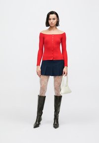 Czerwony prążkowany sweter z odkrytymi ramionami z guziczkami, zestawiony z granatową mini spódniczką, kabaretkami, czarnymi kozaczkami za kolano i białą torebką.