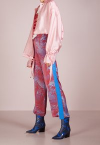 Blusa larga de manga larga metálica rosa con mangas fruncidas, combinada con pantalones de patrón rosa y azul y botines de tacón azul con acentos florales.
