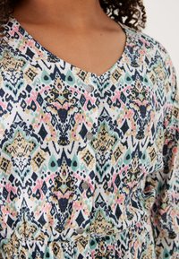 Mehrfarbiges gemustertes Kleid mit V-Ausschnitt, dekorativen Knöpfen und einem weichen, strukturierten Stoff mit komplizierten Designs in Rosa, Schwarz und Petrol.