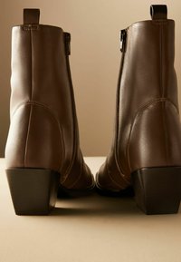 Bottes chelsea en cuir marron avec une texture lisse, des zips sur les côtés et des talons bas, présentant une silhouette élégante et ajustée.