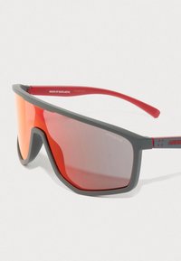 Szare i czerwone sportowe okulary przeciwsłoneczne z lustrzanymi czerwonymi soczewkami oraz brandingiem "Arnette" na zauszniku i krawędzi soczewki.