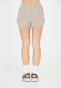Beige Sportshorts mit Seitentaschen, featuring einen elastischen Bund und einem geschichteten Design. Getragen mit weißen Socken und braunen Sneakern.