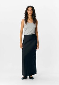 Top senza maniche grigio con scollatura rotonda abbinato a una lunga gonna nera in tessuto liscio, in contrasto con delle scarpe basse nere.
