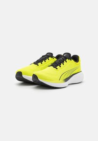 Zapatillas de running de un amarillo brillante con una parte superior de malla texturizada, cordones negros y una entresuela blanca acolchada. Presenta una suela exterior de goma negra.