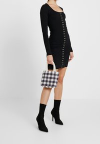 Černé šaty s dlouhým rukávem a předními knoflíky, doplněné o barevnou kabelku s texturovaným kostkovaným vzorem a perlami podobnými úchyty.