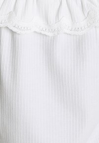 Tissu blanc côtelé avec une délicate bordure en dentelle festonnée en haut. La texture est douce avec des rayures verticales qui accentuent le design.