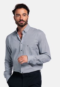Wit button-down shirt met een blauw geometrisch patroon, lange mouwen en een zakdetail op de linkerborst. Draag het met donkere broek.