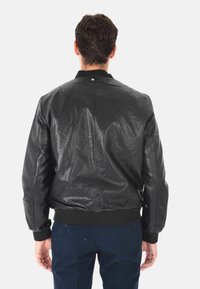 Giacca bomber in pelle nera con polsini e colletto a coste. Texture liscia con una finitura leggermente lucida, caratterizzata da un design sul retro e dettagli di cucitura.
