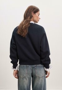Felpa blu scuro con vestibilità comoda, polsini a costine e scollatura rotonda, abbinata a jeans chiari strappati con tasche posteriori.
