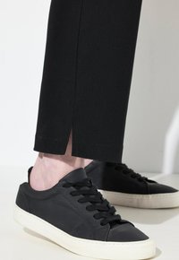Zwarte canvas sneakers met een gestructureerde afwerking, voorzien van zwarte veters en een witte rubberen zool. De broek is zwart en heeft een split aan de zoom.
