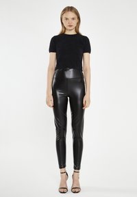 Maglione cropped nero e peloso con leggings in similpelle neri a vita alta, abbinati a décolleté neri con cinturini; vista frontale, sfondo chiaro.