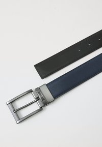 Cinturón bicolor: correa de cuero negro y correa texturizada azul marino. Incluye una hebilla de metal plateado con ranuras horizontales y marca.