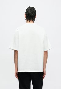 T-shirt bianca oversize con maniche corte, realizzata in tessuto strutturato e con taglio dritto, mostrata su uno sfondo semplice.