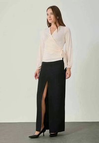 Lys rosa innpakningstopp med lange ermer og knytedetalj, sammen med en svart maxiskjørt med en høyt splitt, iført svarte hæler.