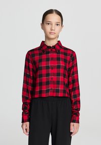 Camicia a quadri rossi e neri con maniche lunghe, chiusura con bottoni e colletto; realizzata in tessuto intrecciato con dettagli di cucitura bianca.