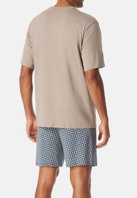 Beige t-paita lyhyillä hihoilla, joka on yhdistetty sinisiin kaavion muotoihin painettuihin shortseihin. Kangas näyttää pehmeältä ja rentoa istuvuutta omaavalta.