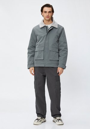 Grijze geïsoleerde jas met een donzige kraag, twee voork pockets, gecombineerd met donkere cargobroek en multi-kleurige sneakers. Eenvoudig, functioneel ontwerp.