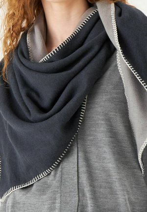 Châle triangulaire bleu foncé et gris en tissu doux, avec des coutures contrastées le long des bords, drapé autour des épaules.
