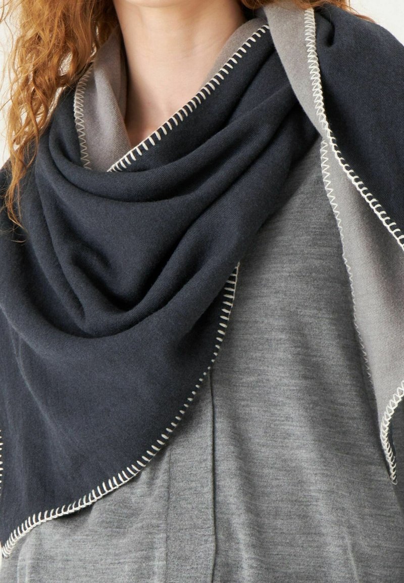 Châle triangulaire bleu foncé et gris en tissu doux, avec des coutures contrastées le long des bords, drapé autour des épaules.
