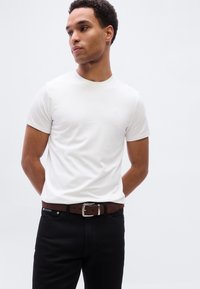 Λευκό κοντομάνικο μπλουζάκι με στρογγυλή λαιμόκοψη, συνδυασμένο με σκούρο τζιν και καφέ ζώνη με ασημί αγκράφα. Απλός και εφαρμοστός σχεδιασμός.