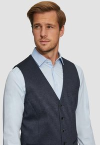 Marine houndstooth textuur vest over een lichtblauwe button-up shirt, met een geknipt kraag en vijf zwarte knopen.