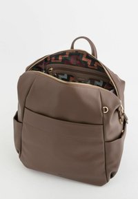 Mochila sintética marrón con textura y herrajes dorados. Cremallera abierta que revela un interior con un patrón multicolor, que incluye un bolsillo con cremallera.