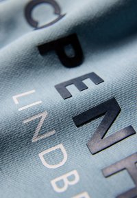 Tela azul claro con una superficie texturizada que muestra grandes letras en blanco y negro. El diseño presenta diferentes estilos y tamaños de letras.