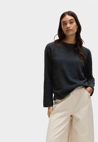 Donkergrijze trui met lange mouwen en een ronde hals, gedragen met lichtbeige broek met wijde pijpen. Zachte textuur en een ontspannen pasvorm.