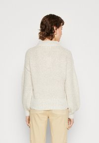 Chunky strikket sweater i off-white med ribbet krave og manchetter. Har en afslappet pasform og tekstureret stof. Bagfra ses sømdetaljer.