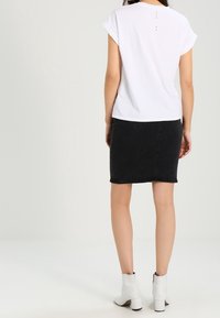 Camiseta blanca de manga corta con puños doblados, que presenta tres pequeños puntos en la parte posterior. Combinada con una falda de mezclilla negra y botines blancos.