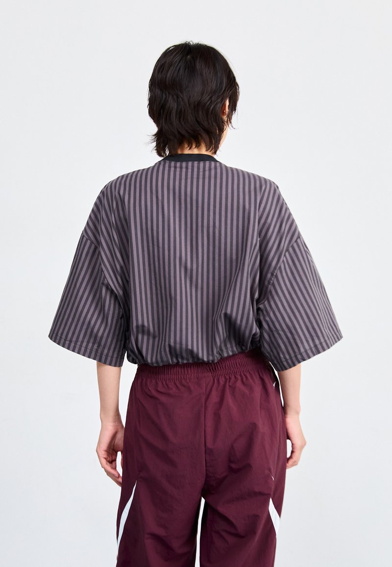 Top a maniche corte grigio a righe con colletto nero, abbinato a pantaloni bordo bordeaux con elastico in vita e dettagli laterali bianchi.