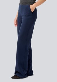 Navy wide-leg trousers with side pockets, smooth texture, and subtle crease details, paired with a fitted top and dark footwear.