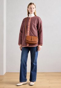 Bruine leren schoudertas, oversized bordeauxrode shirt met patroon en witte accenten, witte coltrui, blauwe jeans, beige ballerina's.