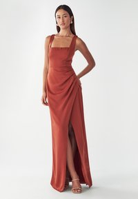 Rostfarbiges, bodenlanges Kleid mit quadratischem Ausschnitt, dicken Trägern, seitlichem Drapé und einem hohen Schlitz bis zum Oberschenkel, aus glattem Stoff.