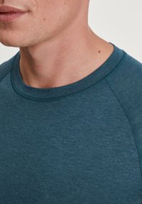 Teal crew-neck t-shirt met een raglanmouwontwerp, gemaakt van zachte, gewatteerde stof. Heeft een gladde halslijn en subtiele stikseldetails.