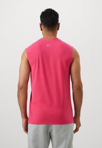 Mouwloos roze sportshirt van katoen, met een ronde hals en een klein wit logo op de achterkant. Soepele textuur; casual pasvorm.