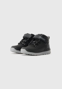 Zapatillas altas Kappa negras con suelas grises, aseguradas con cordones y una correa de Velcro, mostradas lado a lado sobre un fondo blanco.